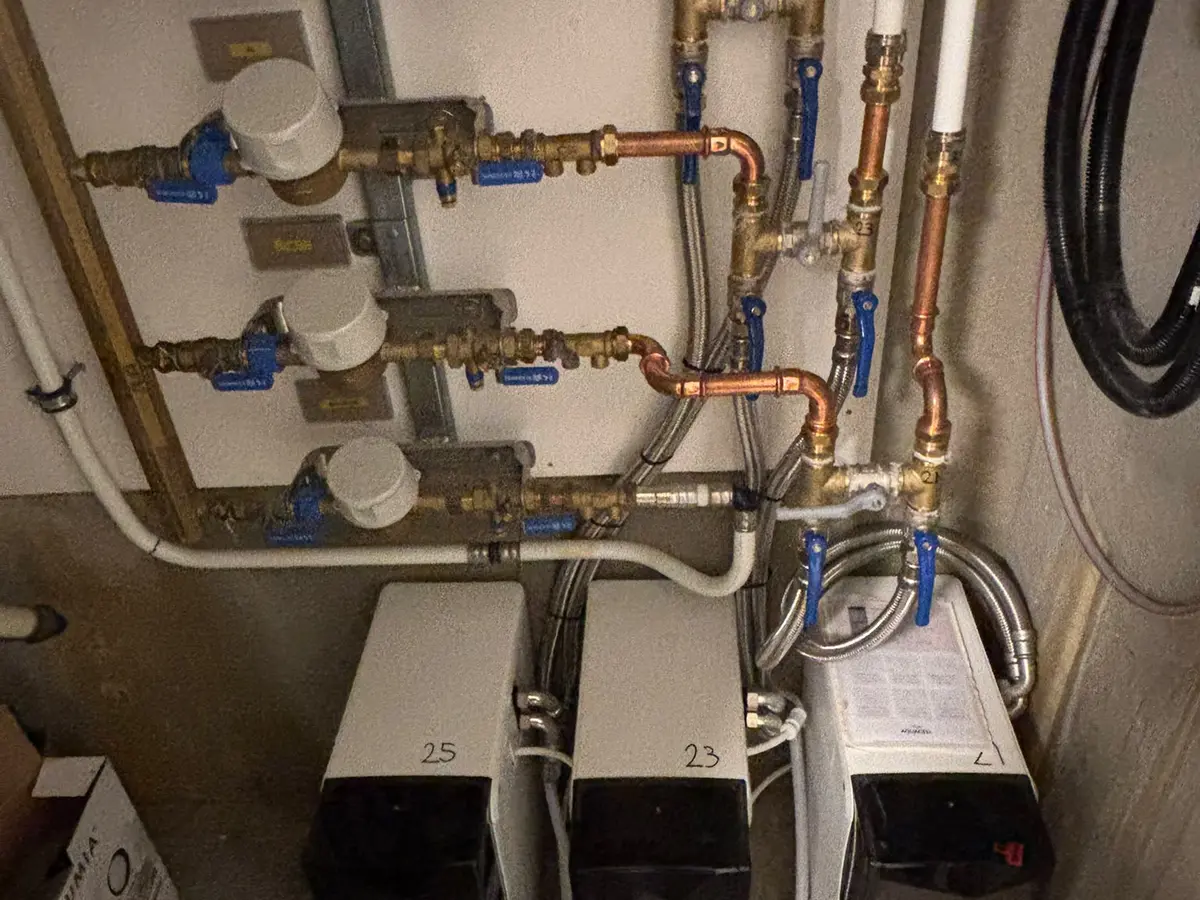 Koperen verdeler met watermeters en cv-aansluitingen in een technische ruimte.